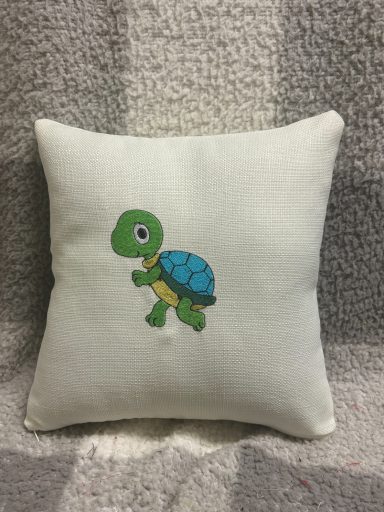 Small cushion with a cartoon turtle design in green and blue on a light background.