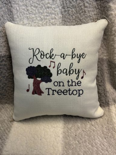 Embroidered cushion with the text "Rock-a-bye baby on the treetop" and a tree motif.