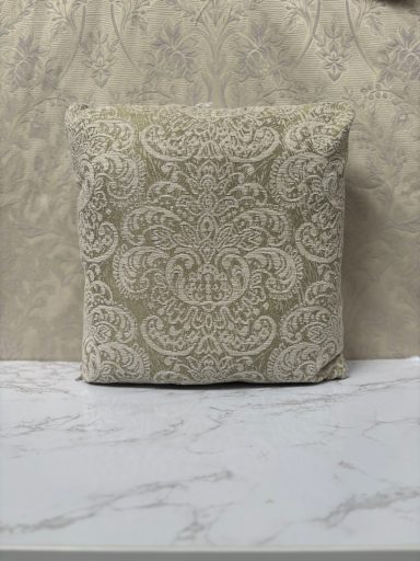 Ornate beige cushion with a floral pattern, placed on a marble surface.