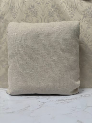 Plain beige cushion on a marble surface, set against a textured background.