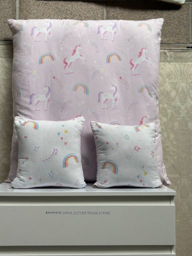 Purple pillow and two smaller cushions with unicorn and rainbow patterns.