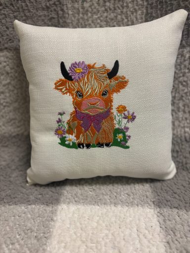 A decorative cushion featuring a Highland cow with flowers and vibrant colours.