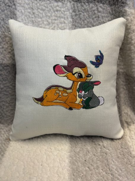 Cartoon deer and rabbit with a bluebird on a decorative cushion.