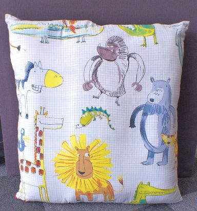 Cushion featuring colourful animal drawings, including a lion, bear, giraffe, and monkey.