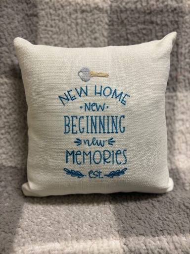 Cushion with the text "New Home, New Beginning, New Memories" in blue on a light background.