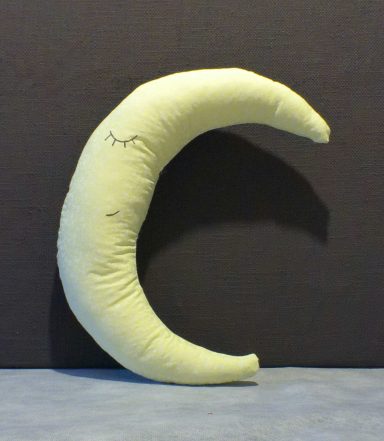 A soft, yellow crescent moon-shaped pillow against a dark background.