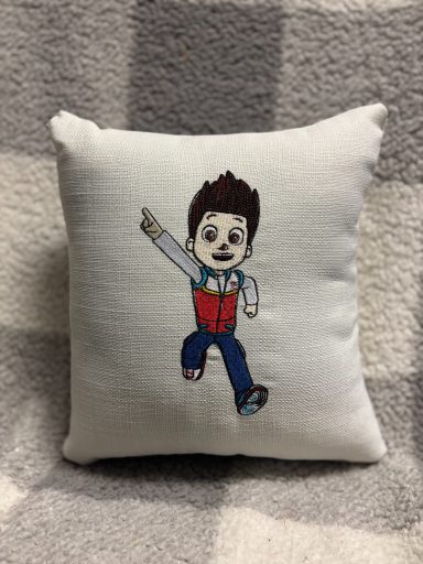 A cushion with a playful cartoon character in a red and blue outfit.