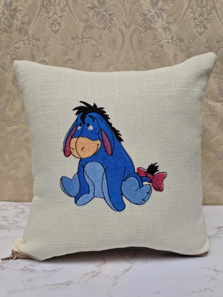 Blue Eeyore character with a sad expression on a cream cushion.