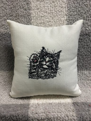 Cushion featuring an embroidered cat with its paw raised.