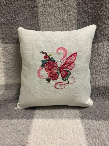 Square cushion featuring a pink butterfly and floral embroidery on a light background.