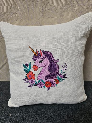 A decorative cushion featuring a purple unicorn surrounded by flowers.