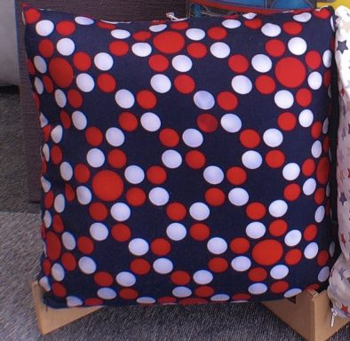 Square cushion with a navy blue background featuring red and white polka dots.