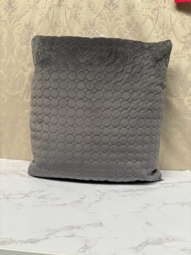 Grey cushion with a textured, geometric pattern resting on a light surface.