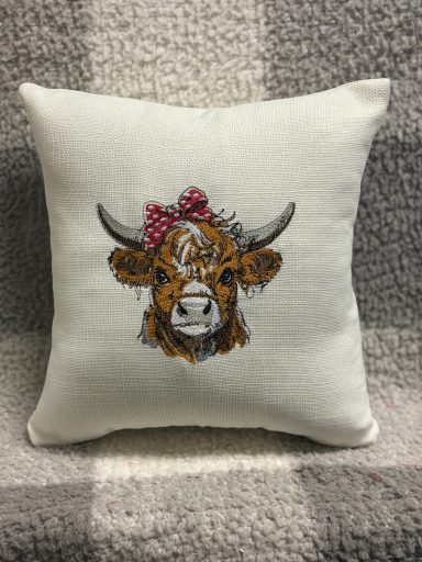 Decorative cushion featuring a Highland cow's head with a red bow.