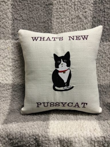 Square cushion with an embroidered black and white cat and the text "What's new Pussycat".
