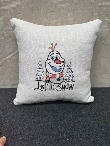 White cushion featuring a cheerful snowman and the phrase "Let It Snow".