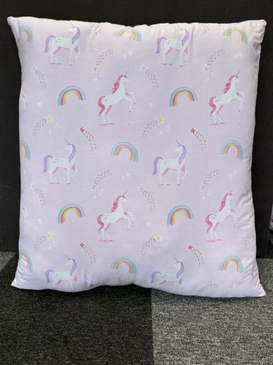 Soft pillow with pastel unicorns and rainbows on a light purple background.