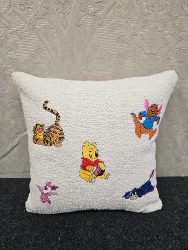 White cushion featuring embroidered characters: a tiger, Winnie the Pooh, and a pink rabbit.