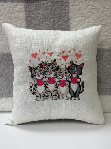 Cushion featuring three cartoon cats with hearts on their chests and love hearts above them.