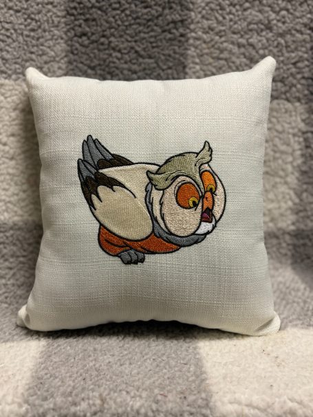 A decorative cushion featuring an embroidered owl design with orange and grey details.