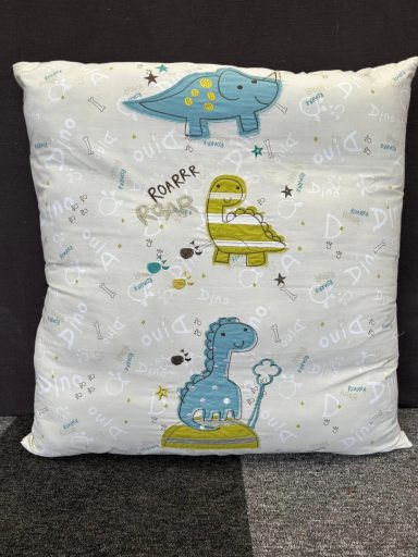 Soft cushion with playful dinosaur and crib illustrations in blue and green.