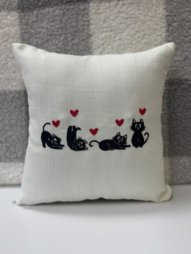 White cushion with black cat silhouettes and red heart motifs.