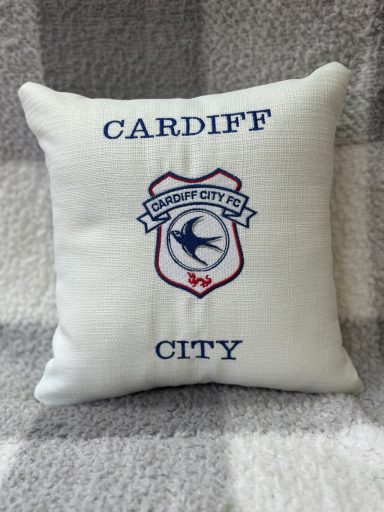 White cushion with "CARDIFF CITY" and a football club crest in blue and red.